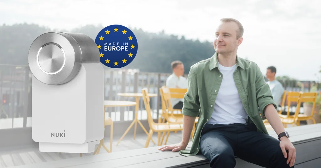 The Nuki Smart Lock Go with a "Made in Europe" badge. In the background is a man in a café.