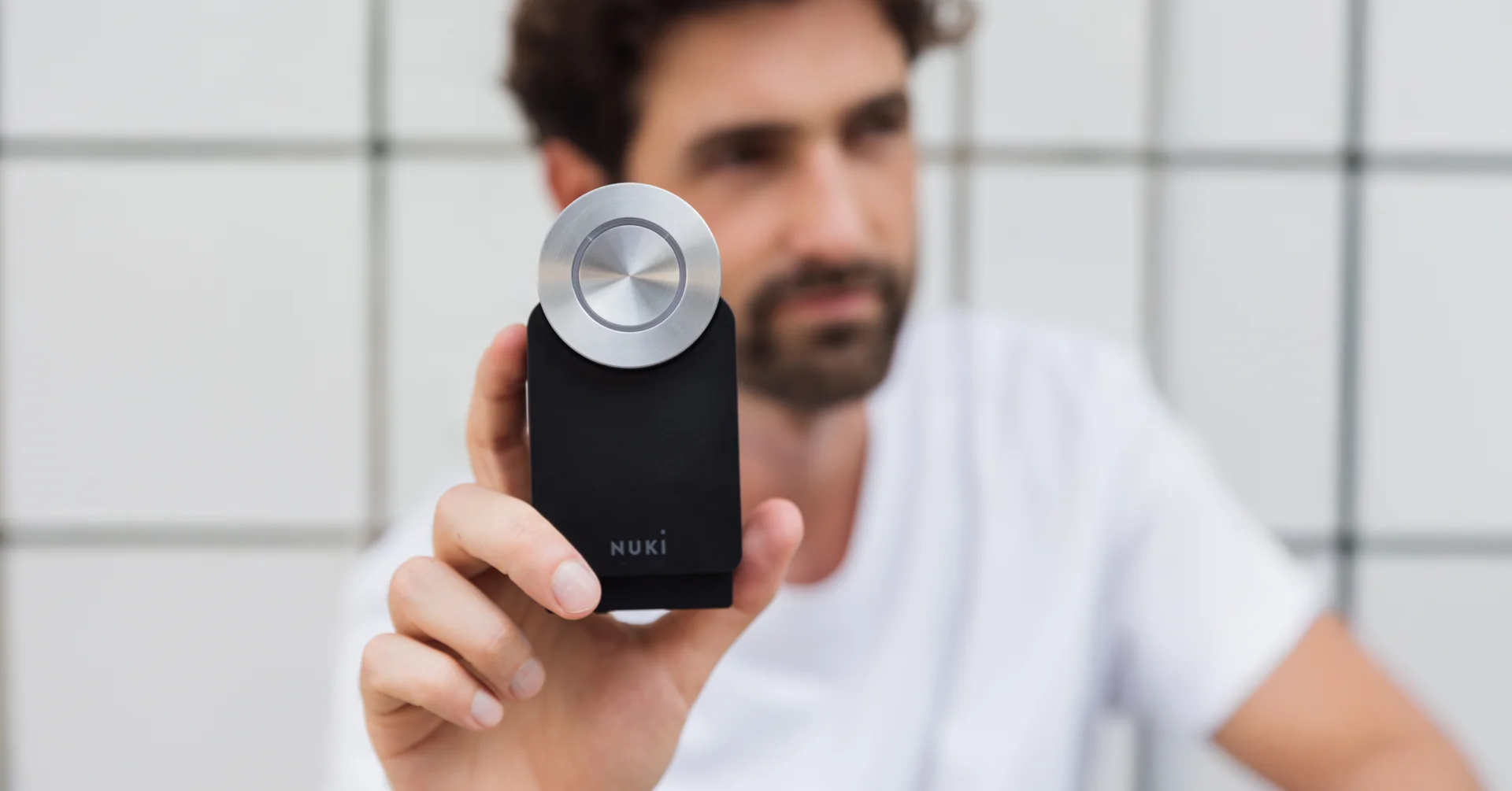 A man in the background holds the Nuki Smart Lock 4th generation in his hand.