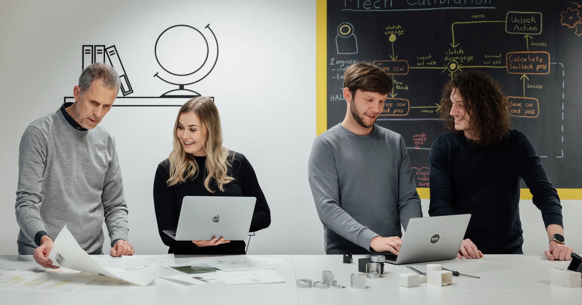 Three men and a woman working together on a project in a room with Smart Lock pieces on the table. 