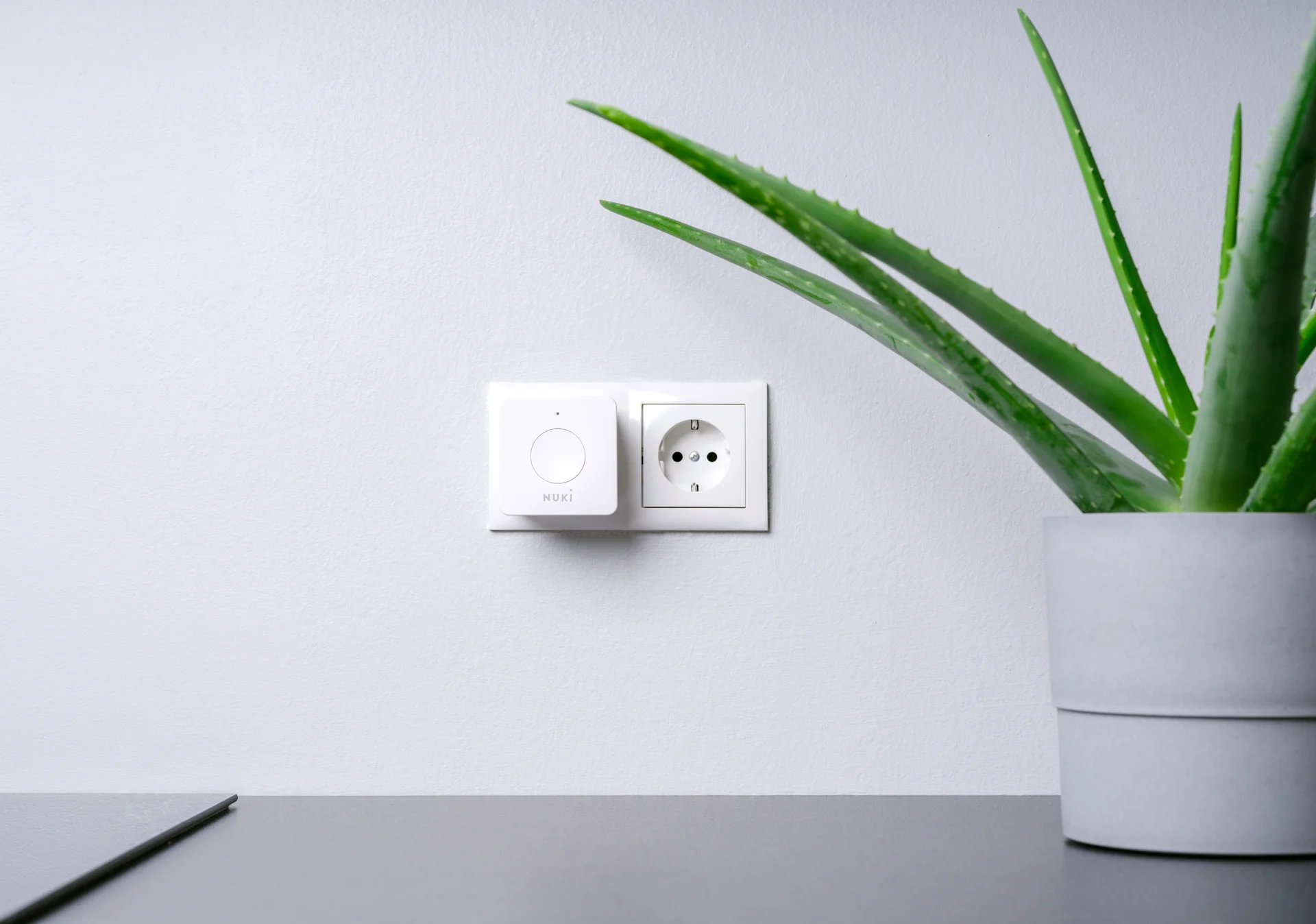 White Nuki Bridge plugged in next to a socket on a white wall – for remote access to your smart lock.