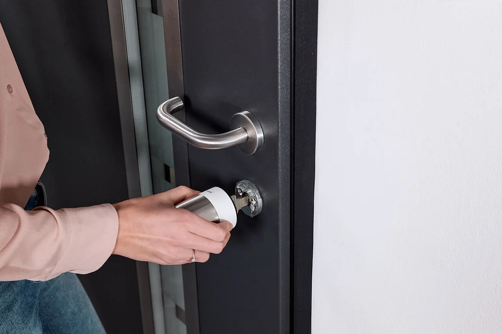 A woman mounts the Nuki Smart Lock Pro with a white ring on a black door.
