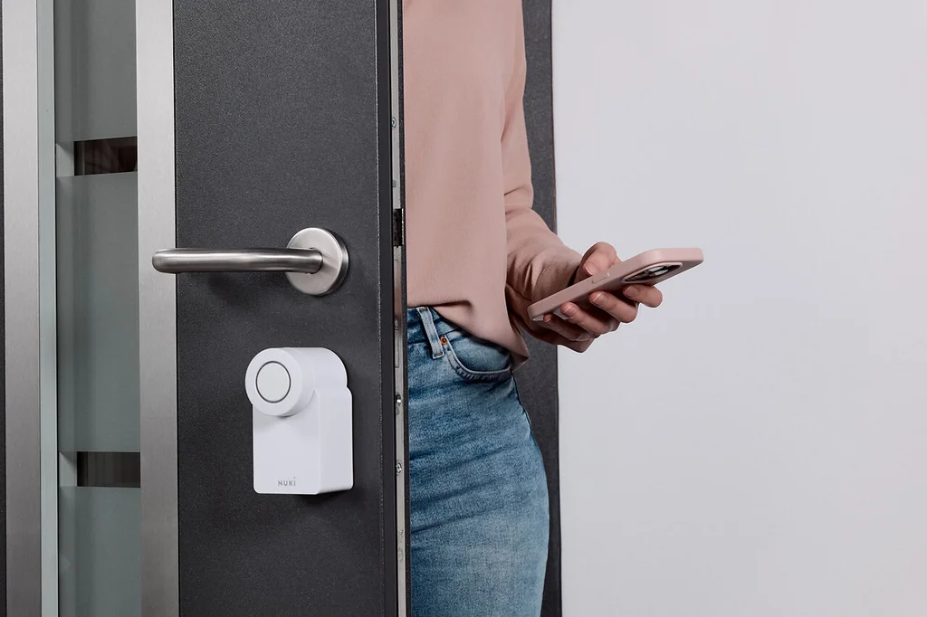 A woman enters a room with her phone in hand and a Smart Lock Go mounted on her door.