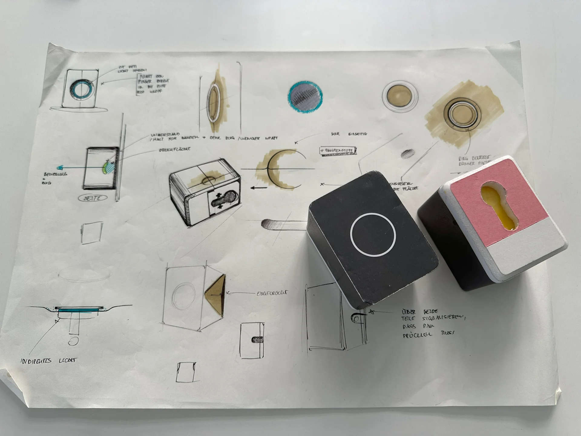 Early drawings of Smart Lock designs on paper with 2 prototypes on top.