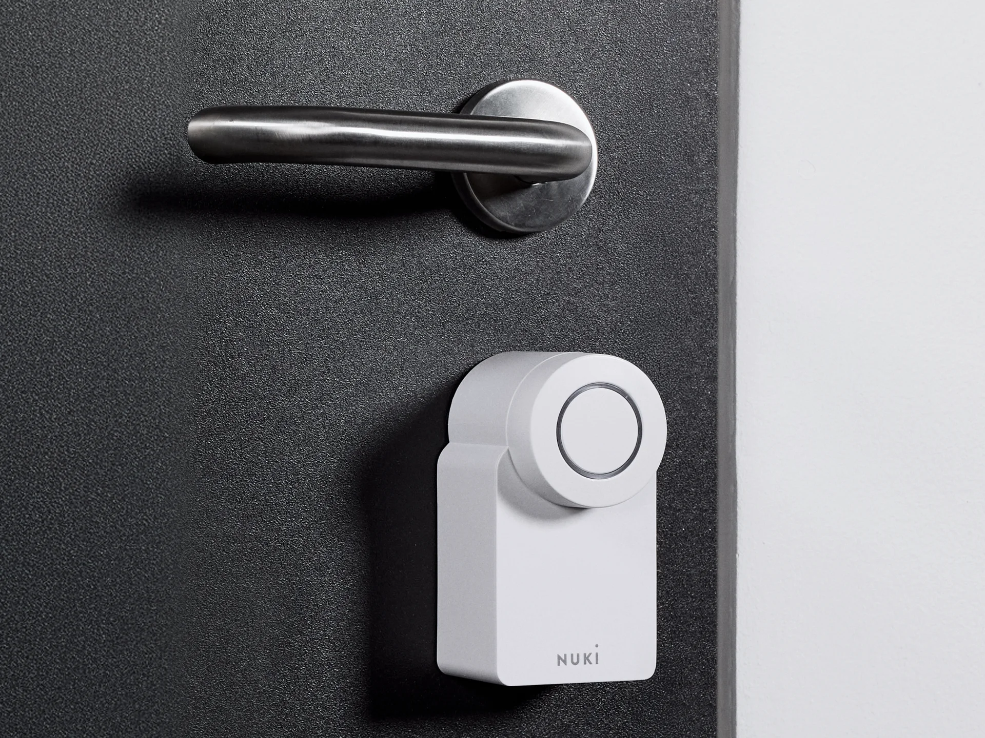 The Nuki Smart Lock Go mounted on a dark door with silver hardware.